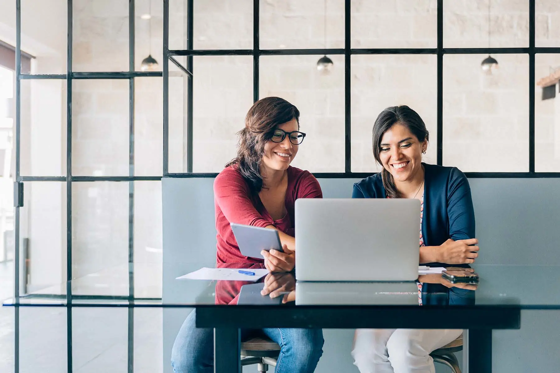 Dos compañeras de trabajo mirando una laptop en una sala de conferencias.