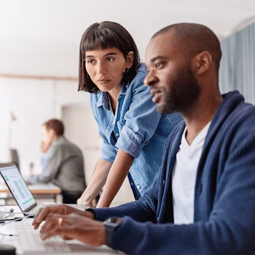 Dos personas colaboran en una computadora, revisando documentos de Docusign en un entorno de oficina moderno.