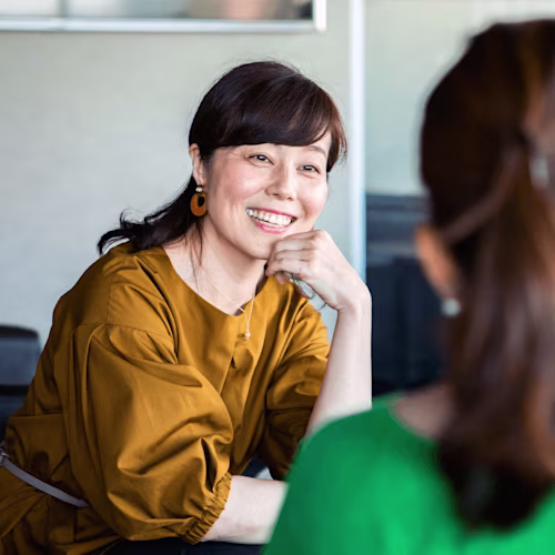 茶色の服を着た女性が考え込んでいる様子。Docusignのビジネスシーンを表現。