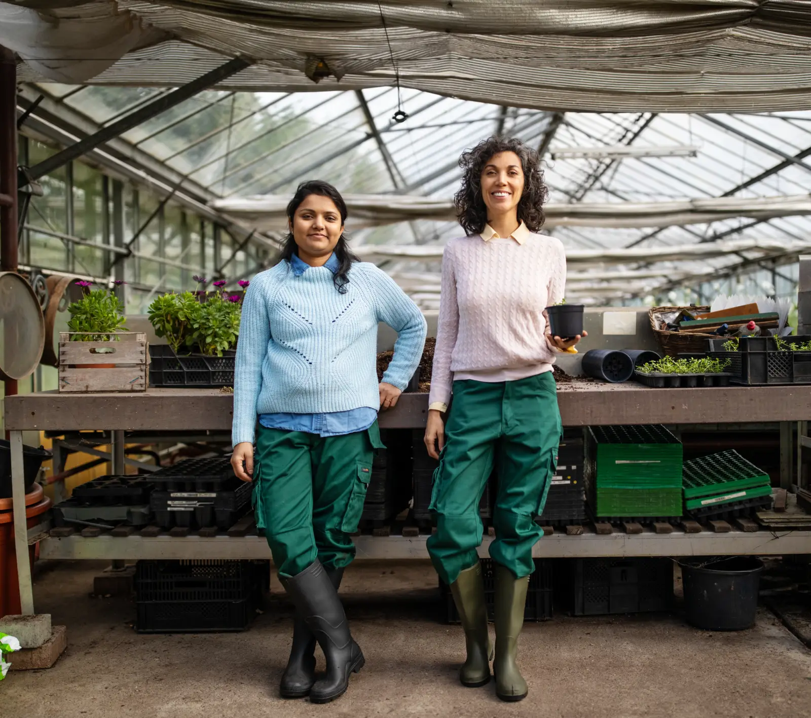 Two woman standing in a greenhouse, smiling at the camera.