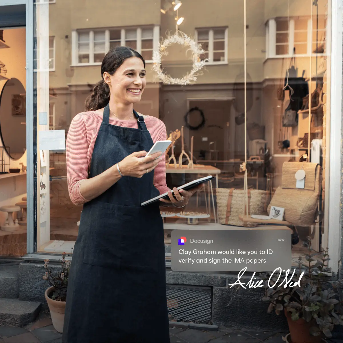 Person holding a phone and tablet smiling outside a small business
