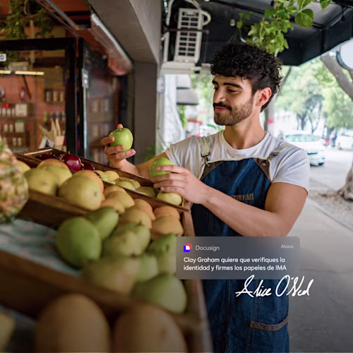 Una persona sosteniendo un teléfono y una tableta sonriendo afuera de una pequeña empresa.