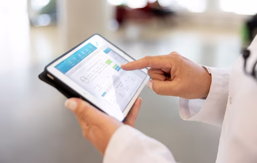 Een zorgprofessional in een witte jas gebruikt een tablet en tikt op een digitale patiëntenregistratie-interface.