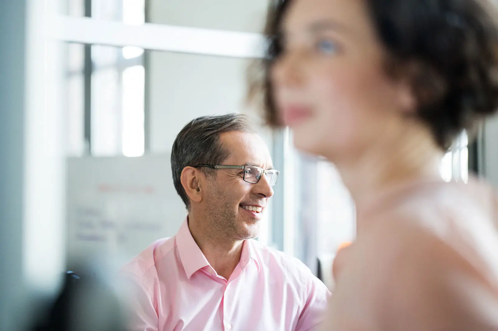 Smiling mature businessman looking away with businesswoman in foreground at office