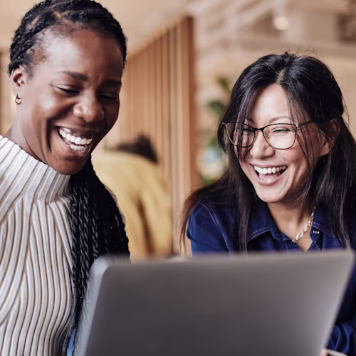 Happy female business professionals sharing laptop at coworking office