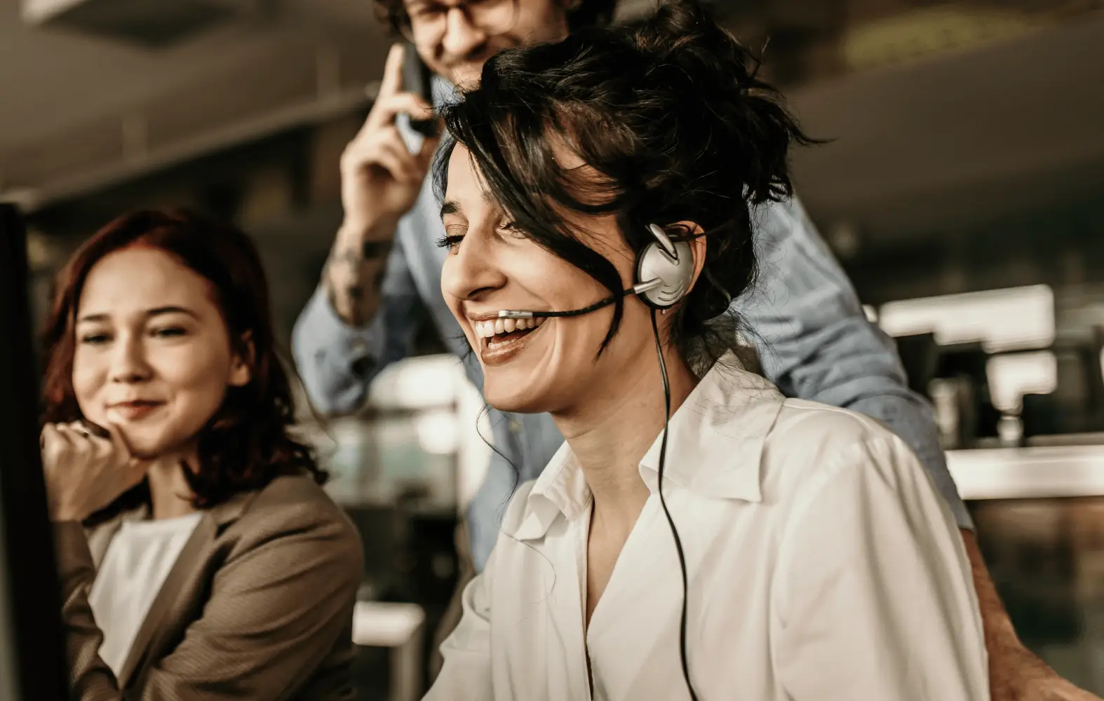 Three IT department employees smile while working, with one of them talking on a headset