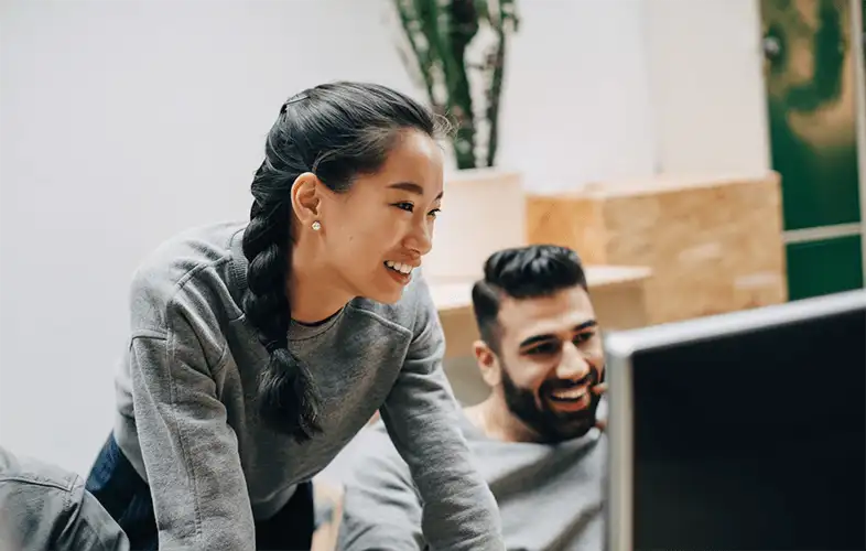 Two coworkers looking at the computer screen and smiling