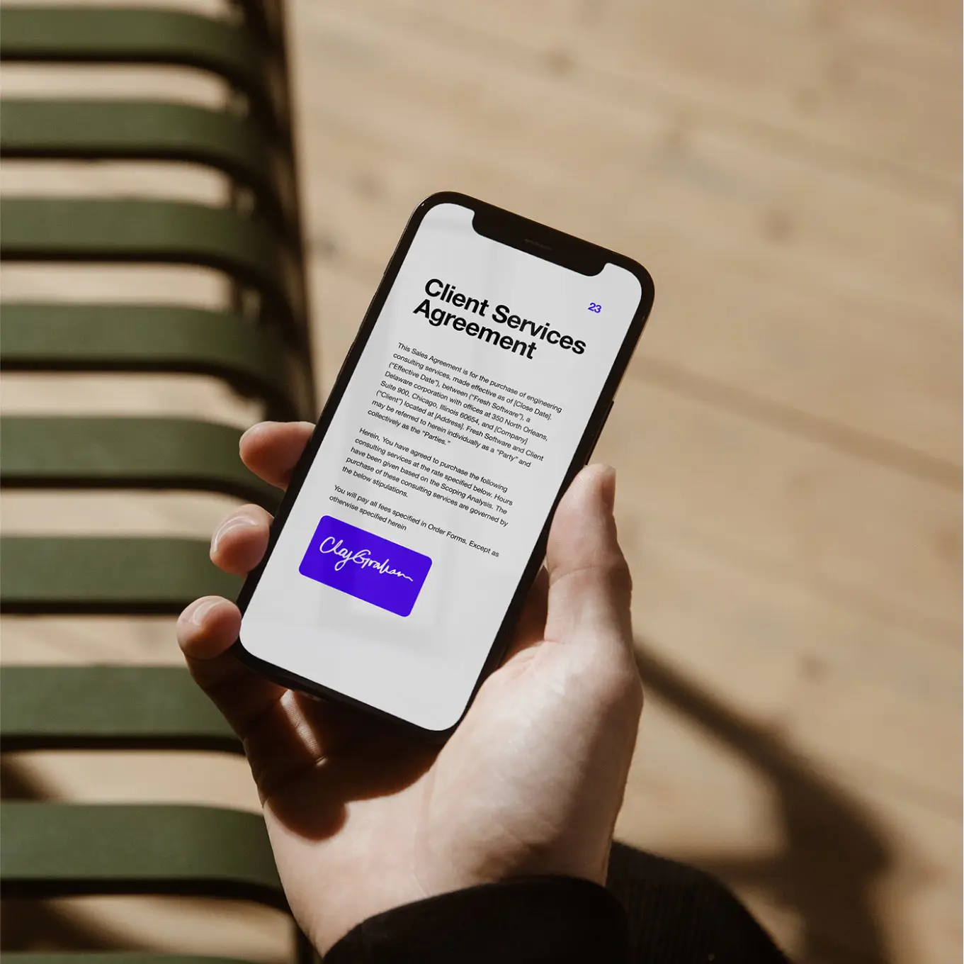 A hand holding a phone showing a client services agreement in Docusign 