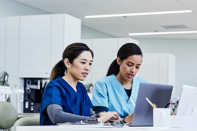 Dos enfermeras sentadas frente a sus computadoras escriben notas