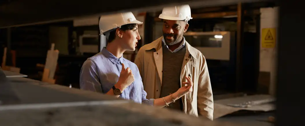 Two people in hard hats discuss a construction project