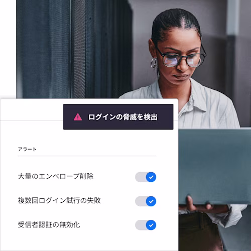 DocuSignが不正ログインの可能性を検知したことを知らせるアラート画面表示が、ラップトップを覗き込んでいる女性の上に重なっている