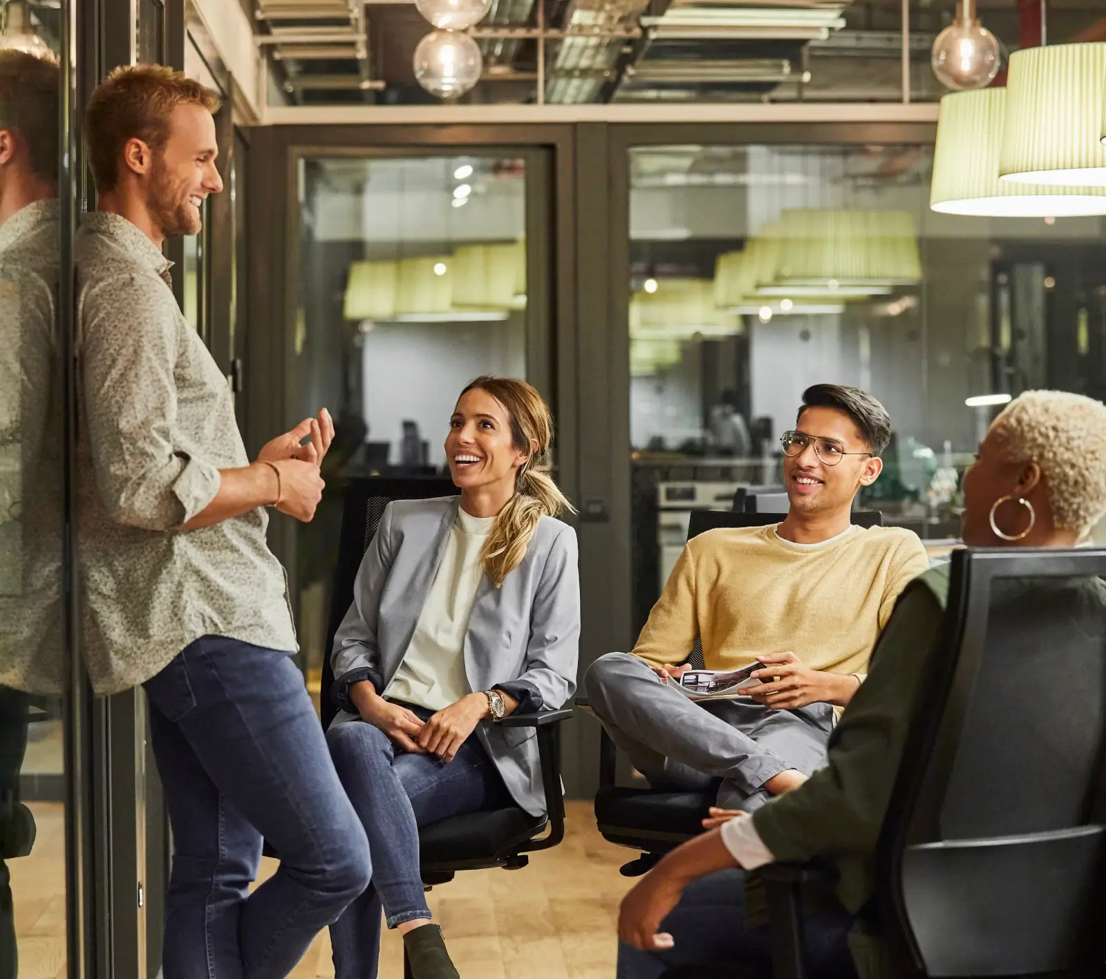 Quatre collègues discutant et souriant dans un environnement de bureau.