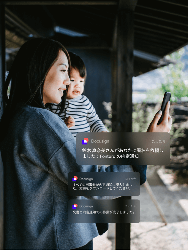 赤ちゃんを抱きながらDocuSign eSignatureから届いたモバイル通知を確認する女性
