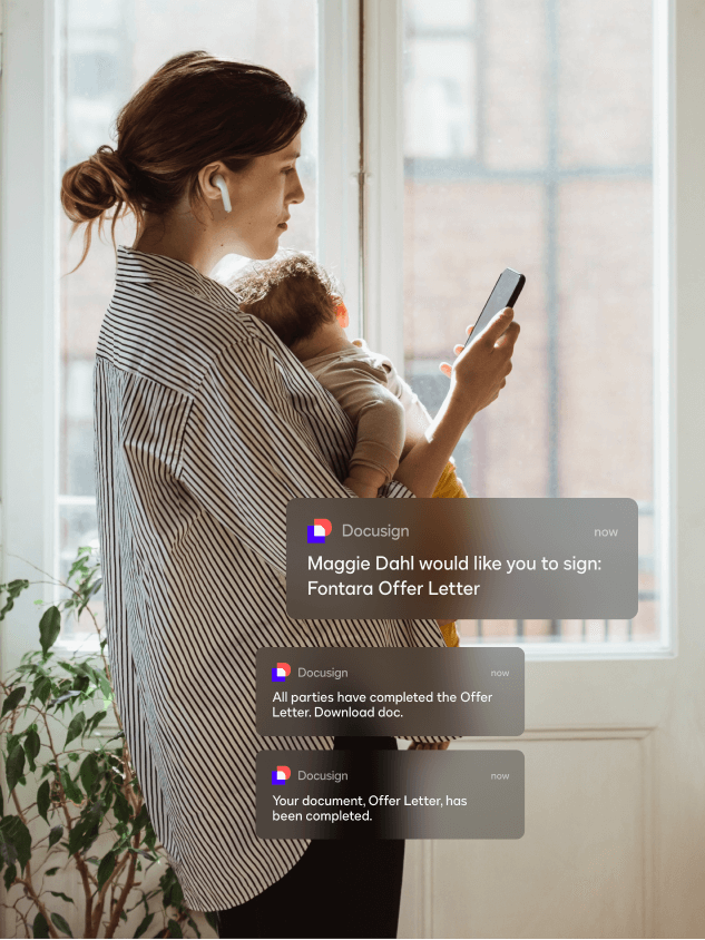 A woman holding a baby and looking at her phone sees mobile notifications for DocuSign eSignature