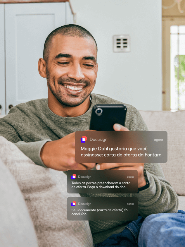 Homem sentado à mesa usando seu telefone para ler notificações móveis do DocuSign eSignature  