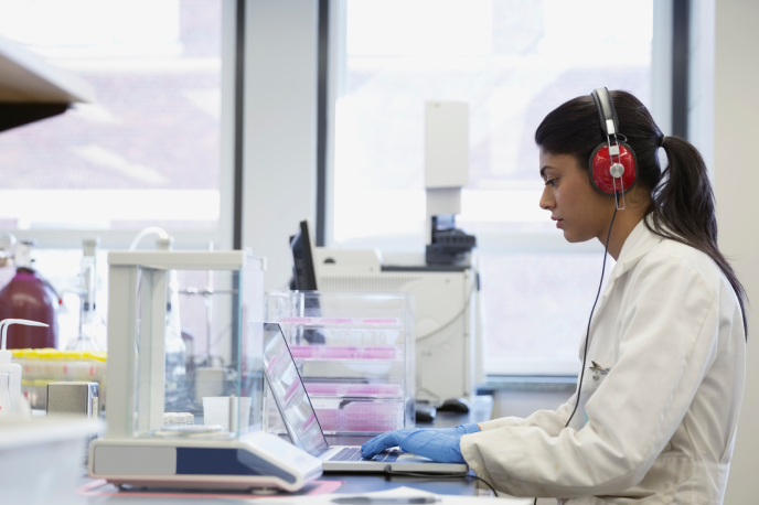 A scientist in a lab coat and latex gloves typing on laptop
