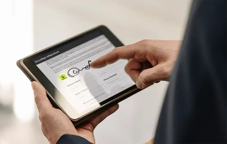 Imagem de perto de mãos segurando um tablet e assinando um documento 
