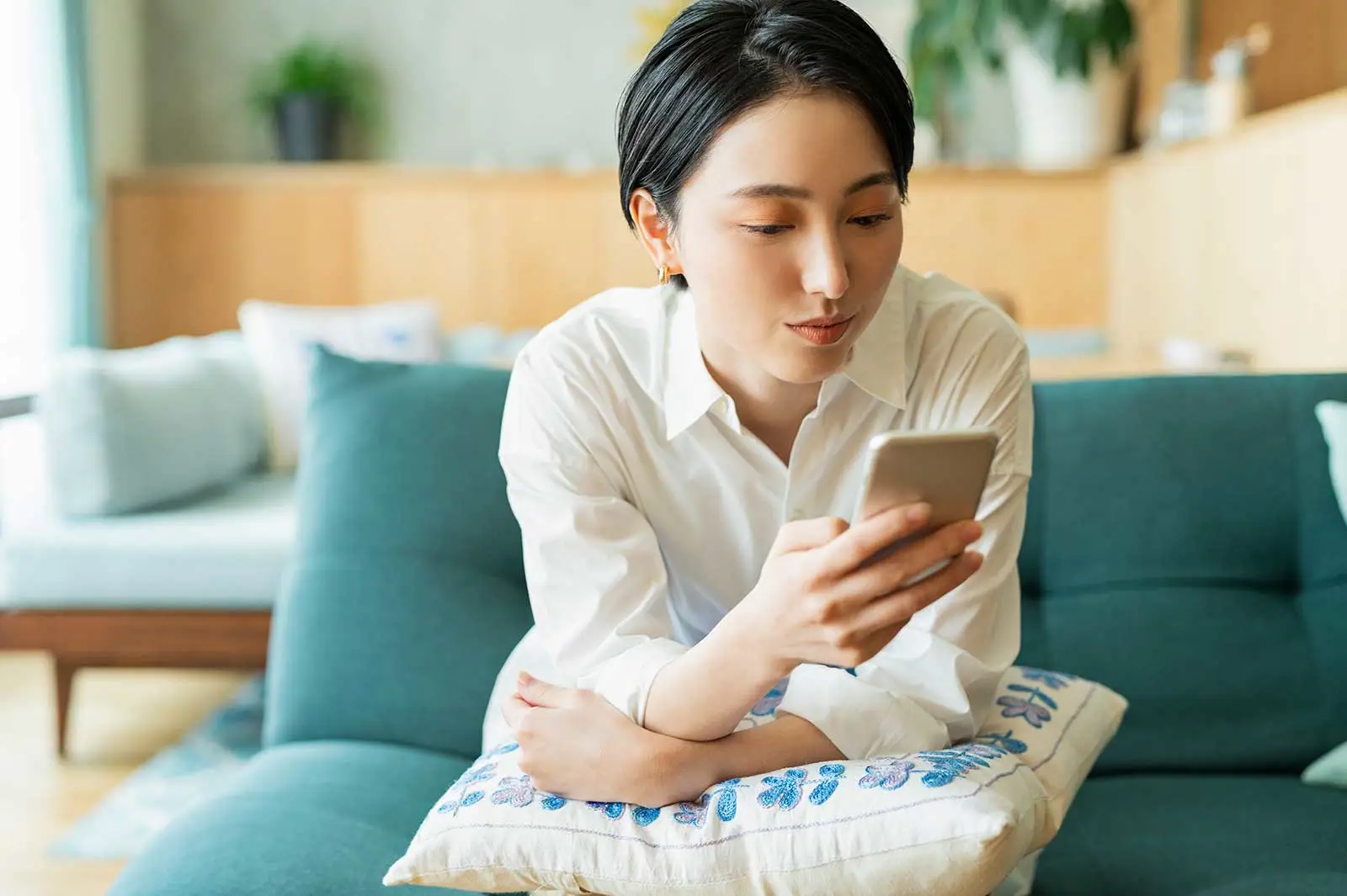 自宅のソファに座ってスマートフォンで情報を検索する女性