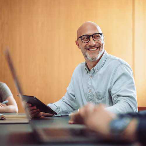 A man is sitting at a table with a tablet and smiling