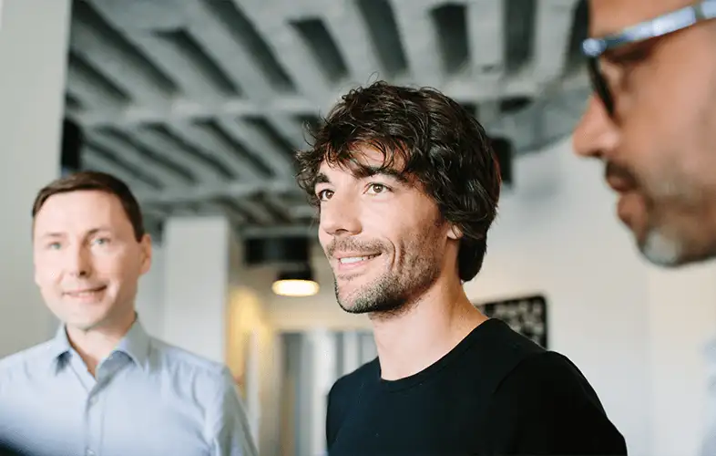 Young men smiling surrounded by co-workers