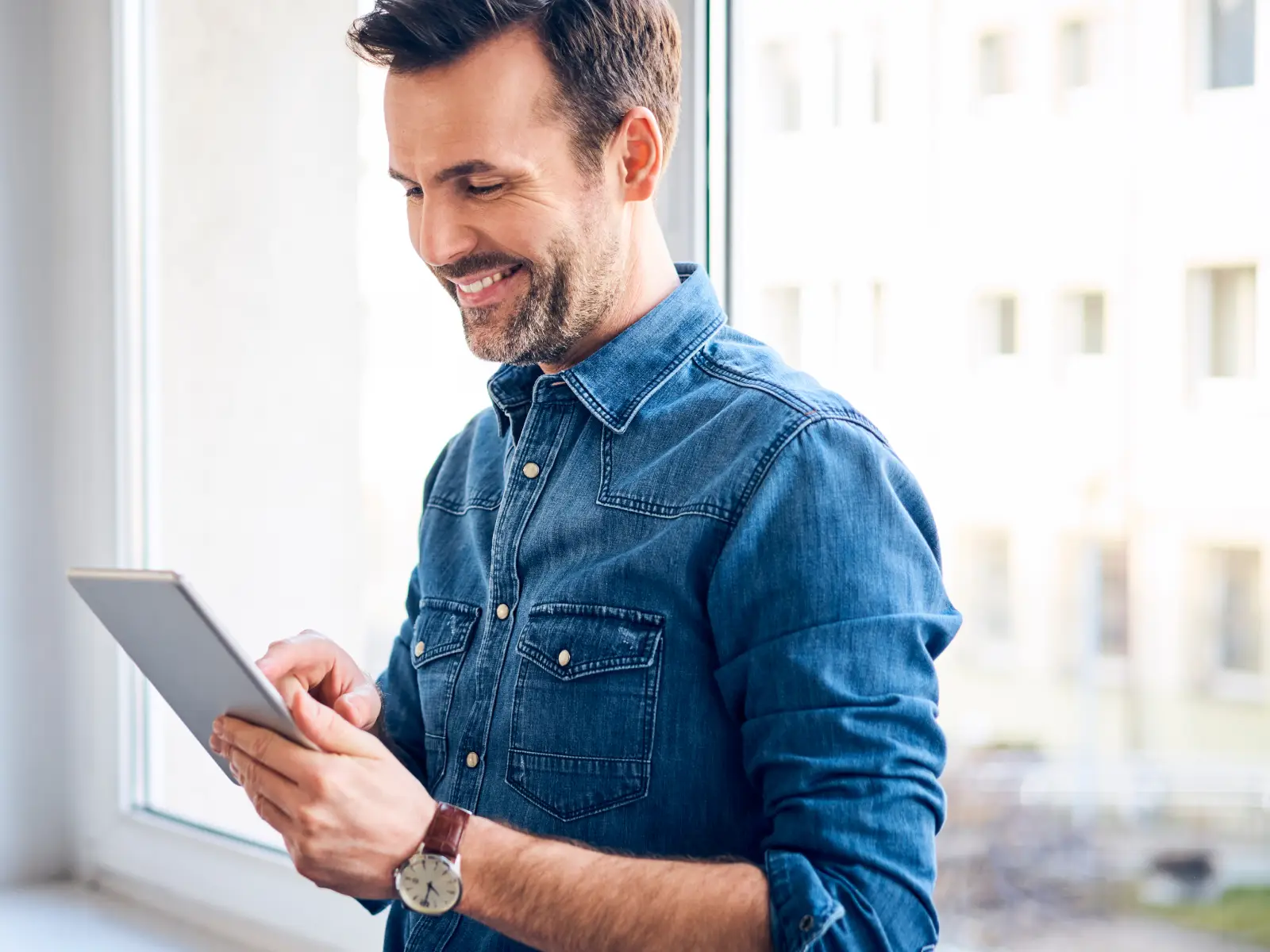 Homem sorrindo enquanto segura um tablet e interage com a tela