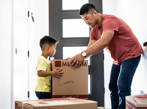 A father and his young son hold a cardboard moving box.