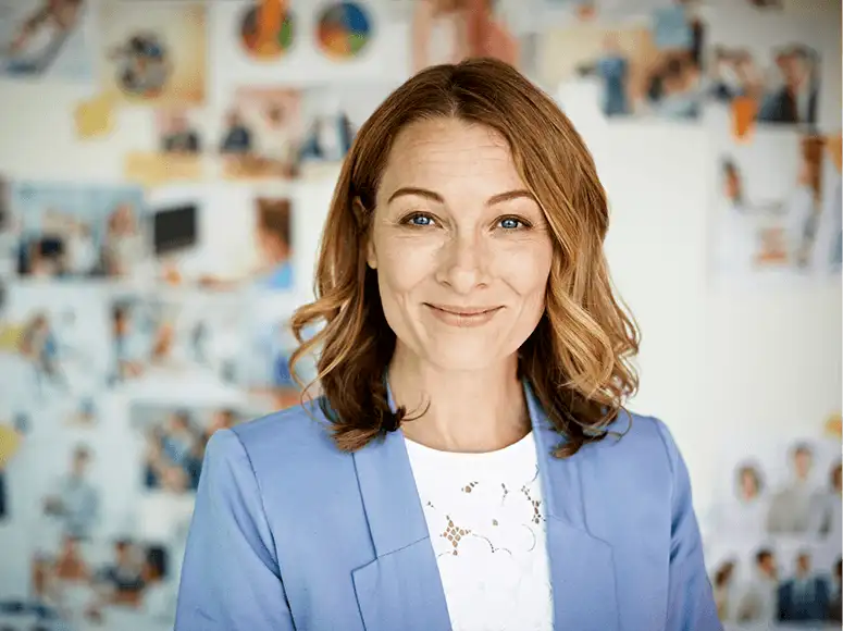 Woman in blue blazer smiling, printed photos on the wall in soft focus behind her