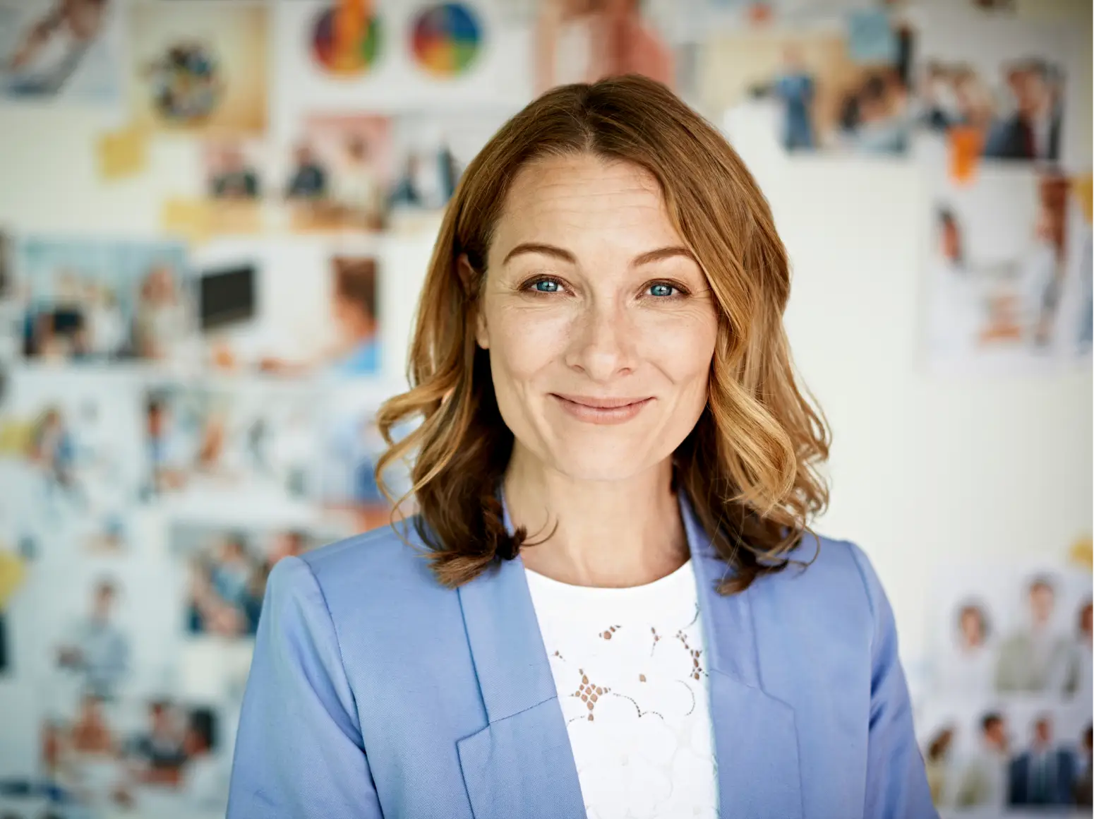 Woman in blue blazer smiling, printed photos on the wall in soft focus behind her