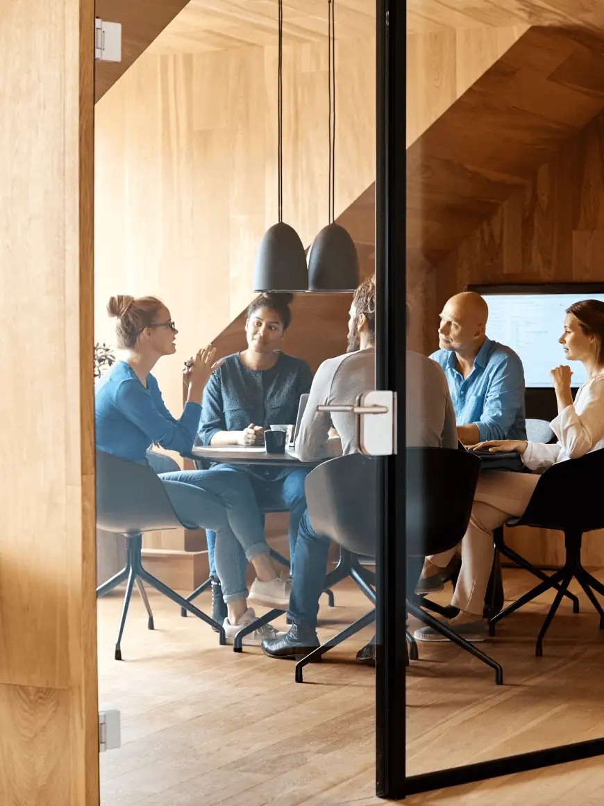 5 miembros de un equipo colaborando en una oficina de madera sentados en la mesa
