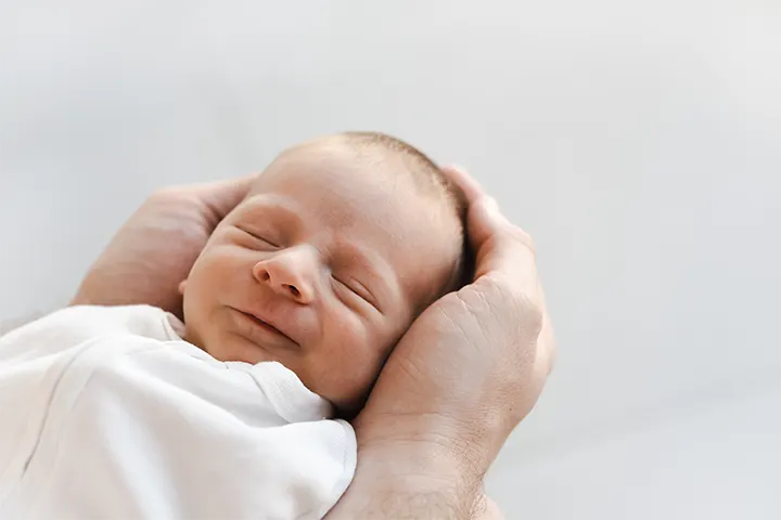 Αντρικά χέρια κρατάνε το κεφαλάκι μωρού που κοιμάται