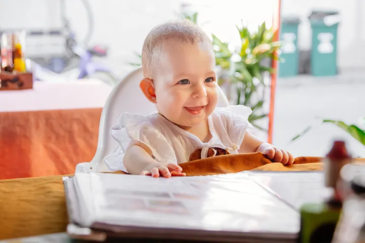  Μωρό κάθεται σε καρεκλάκι φαγητού και χαμογελάει.​