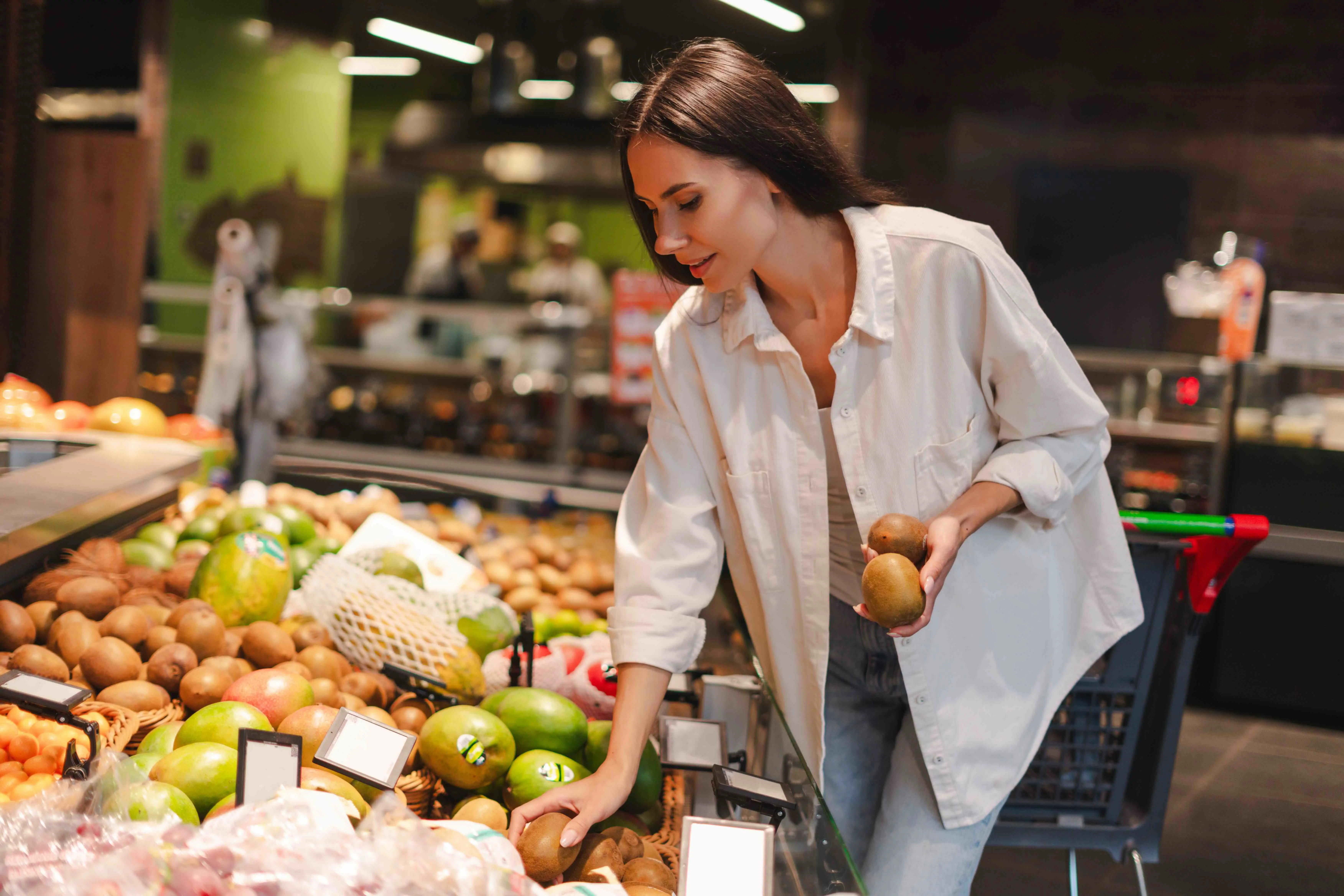 woman choosing kiwi fruit in grocery store