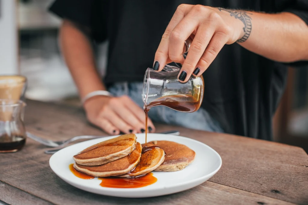 Woman pouring maple syrup on pancakes