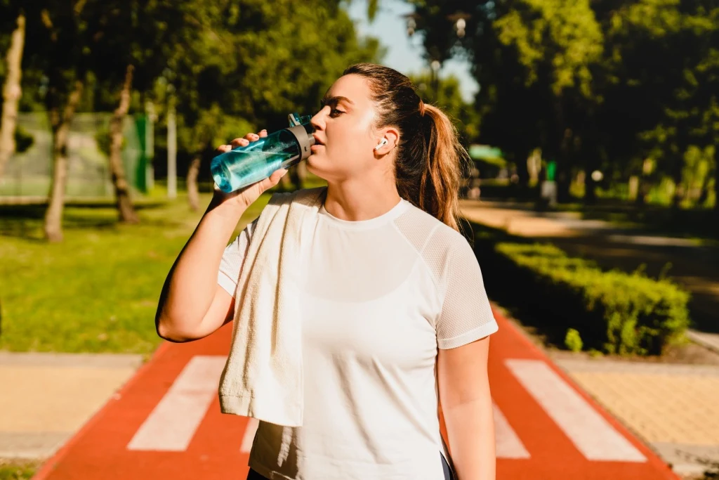 Woman with towel drinking water bottle