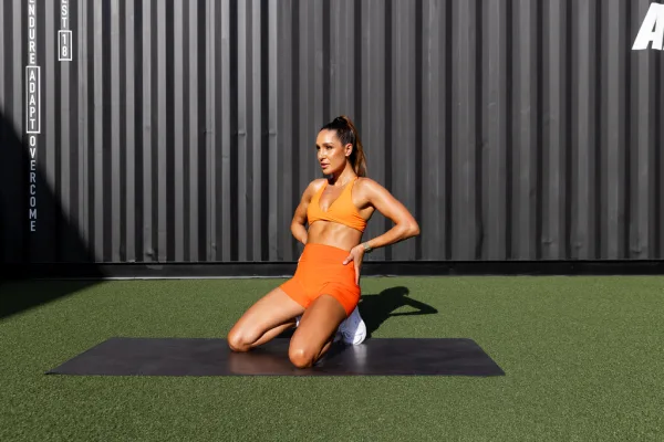 Kayla Itsines kneeling in orange set