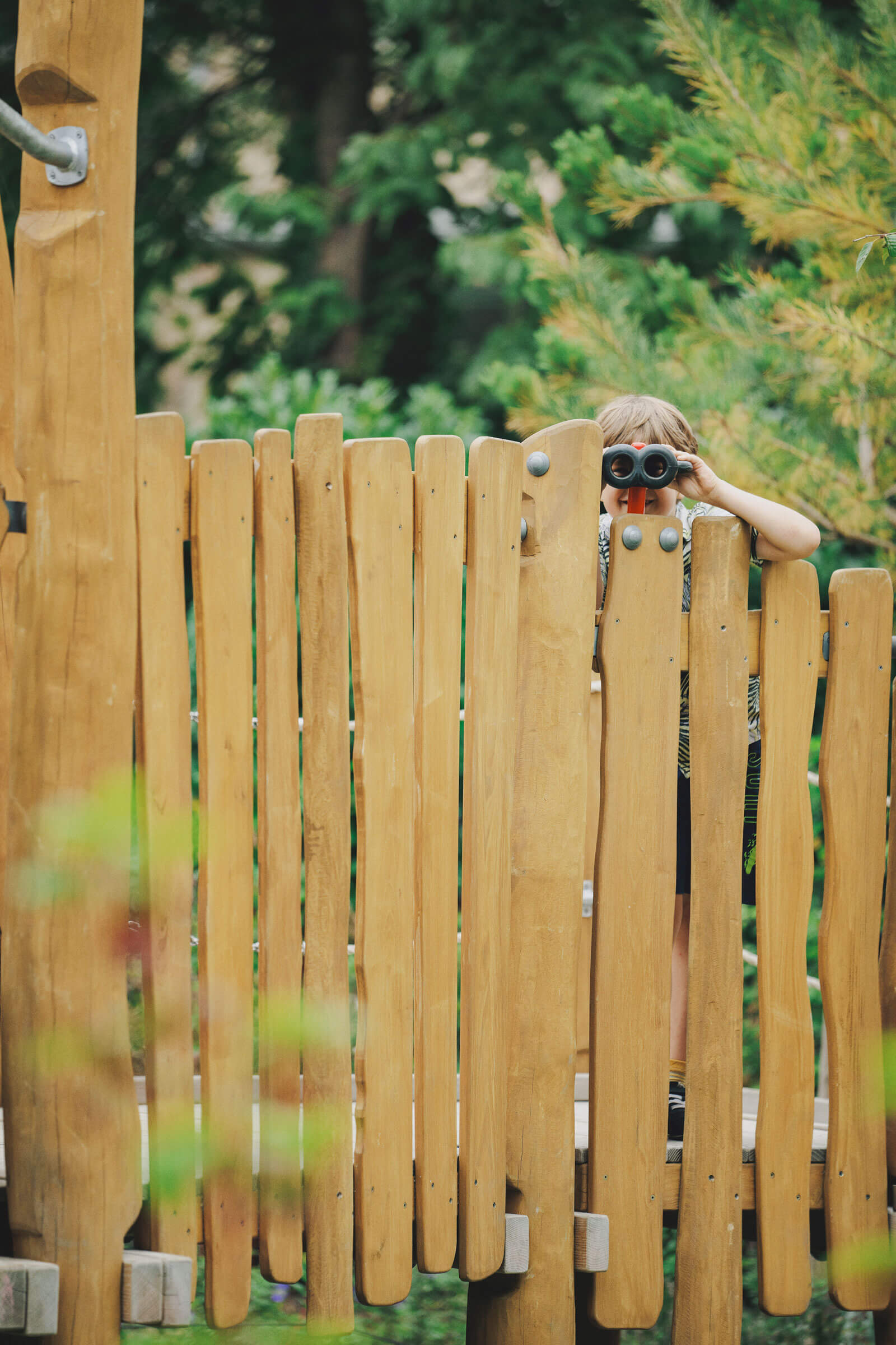 girl looking through binoculars on a wooden playground