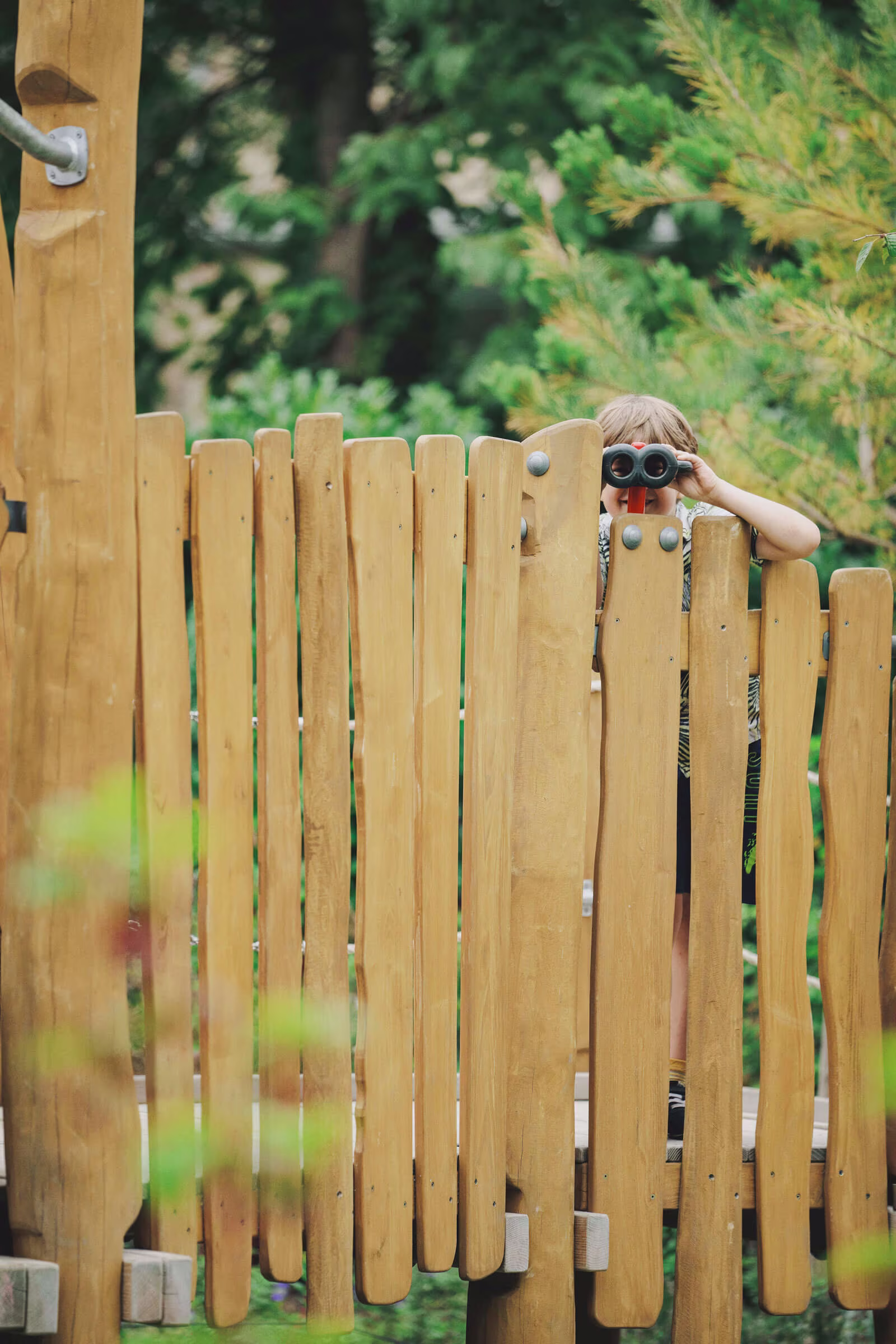 girl looking through binoculars on a wooden playground