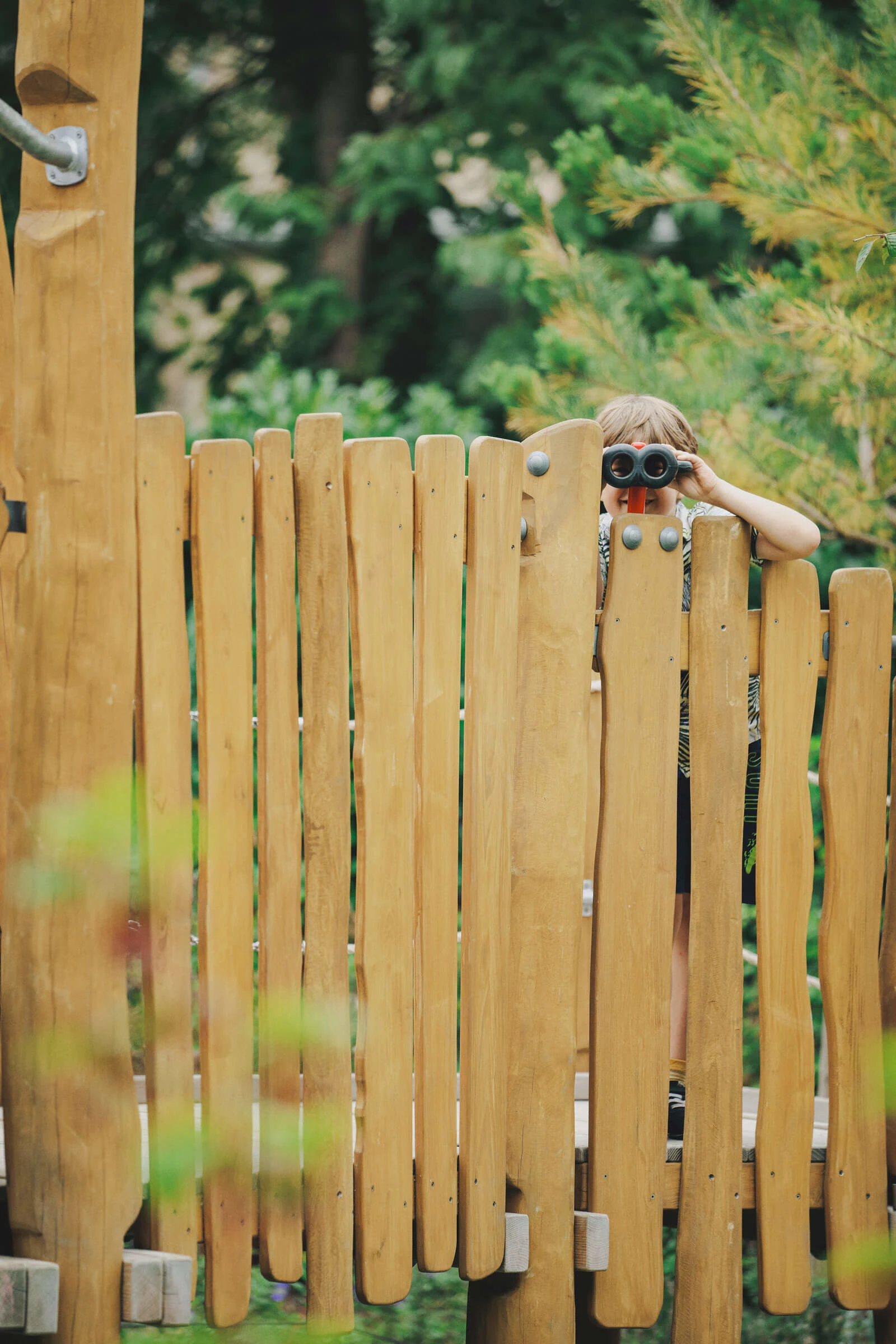 meisje kijkt door een verrekijker op een houten speelplaats