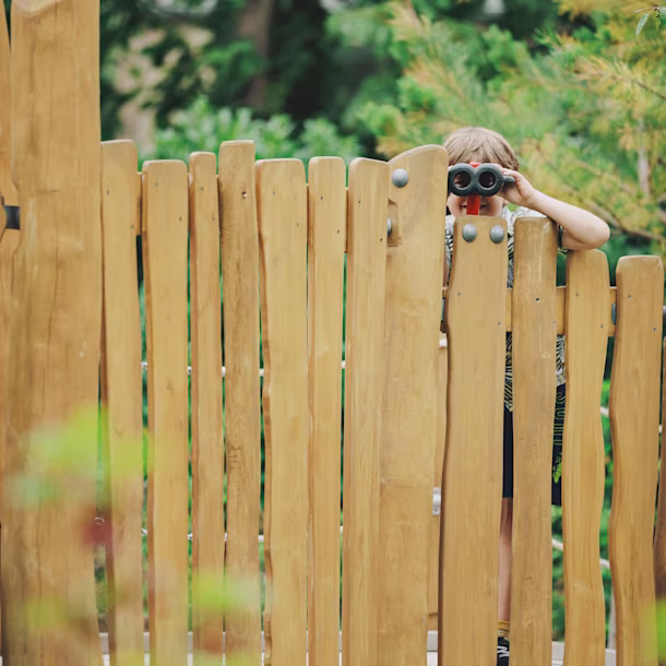 girl looking through binoculars on a wooden playground