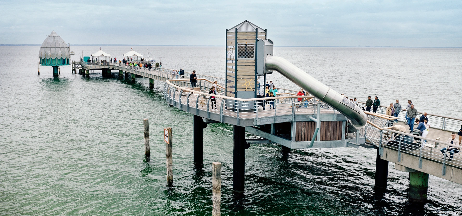 Spaziergänger auf der Seebrücke von Grömitz mit einem speziell angefertigten Spielturm mit Rutsche
