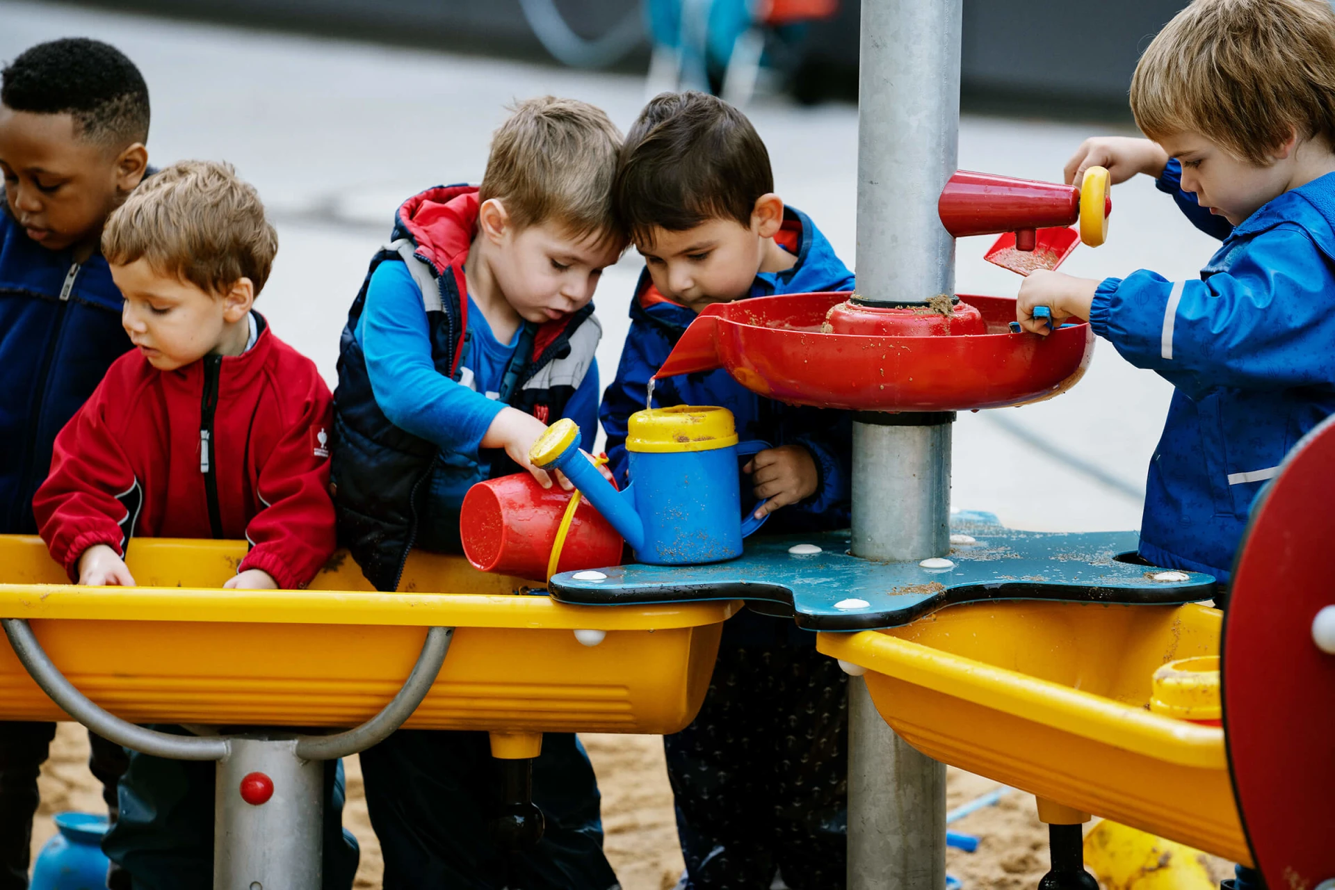 Preschool children using sand and water tables for sensory play. When playground planning, you should consider creating zones for different age groups. Sensory play is great for younger children and those with additional needs. 