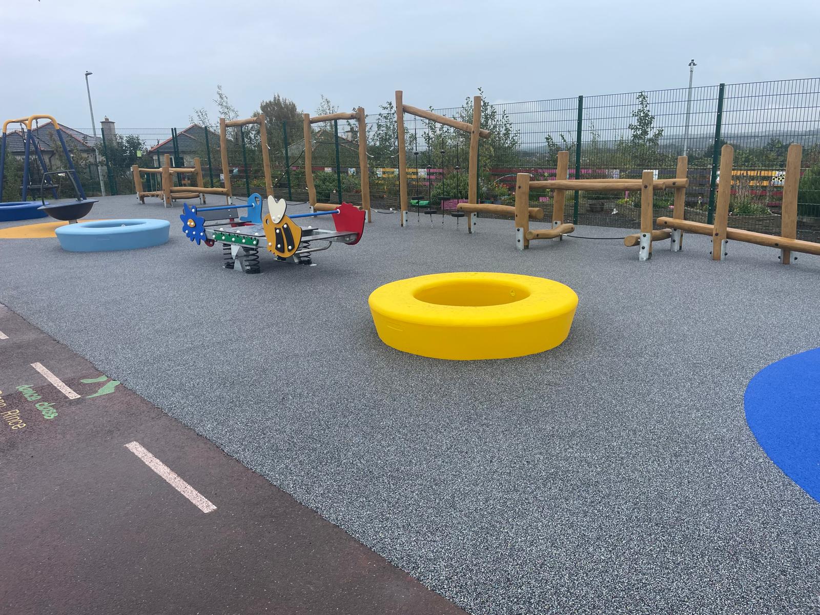 Child using a yellow walker on an accessible playground, wearing leg braces and a cap, with trees and equipment in the background.