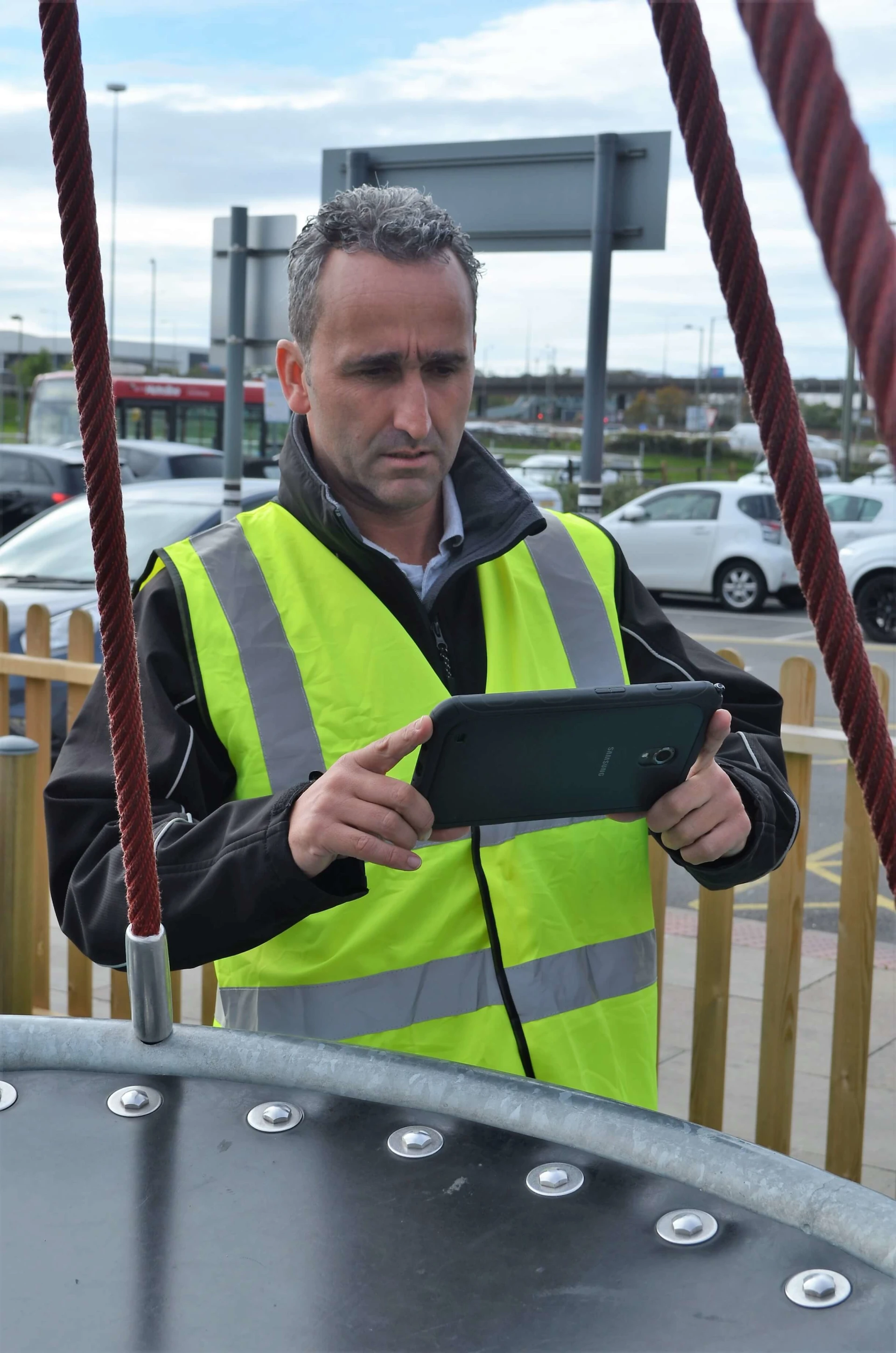 A man wearing a yellow vest maintaining a playground