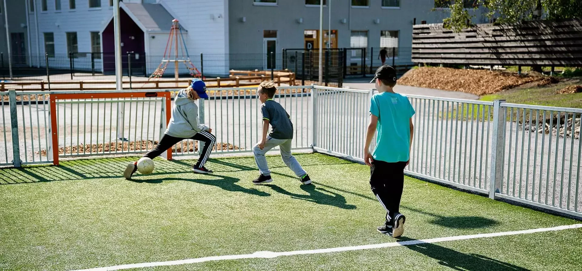 barn spelar fotboll på en multiarena vid en skola