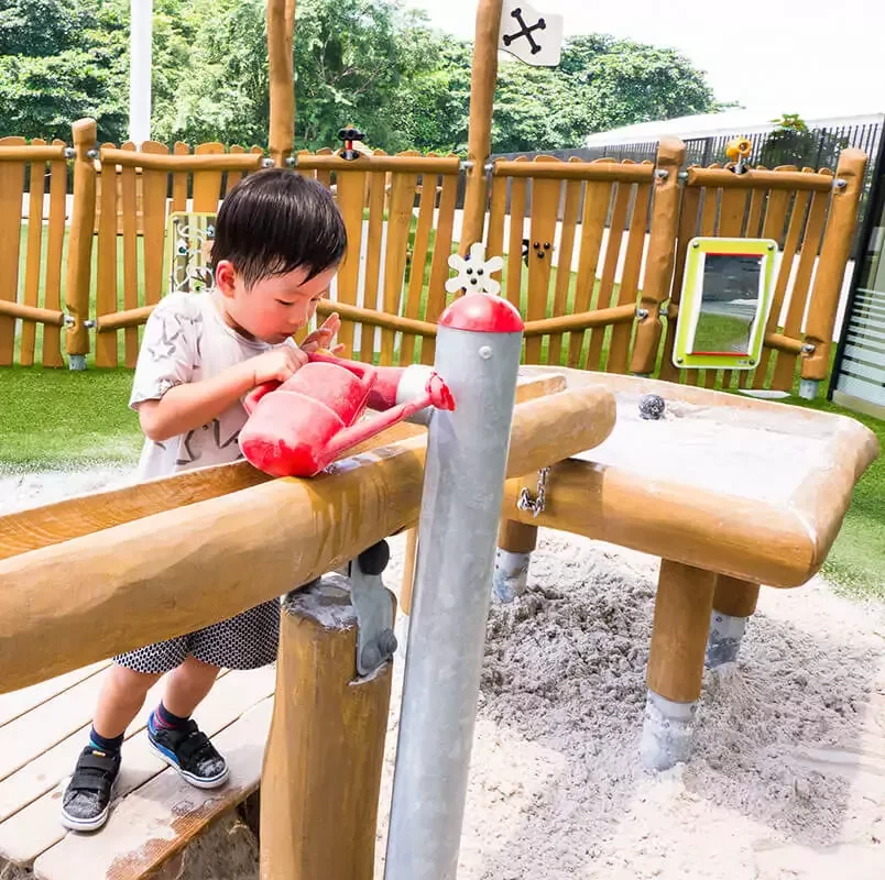 lapsi leikkimässä robiniapuusta valmistetulla hiekka- ja vesileikkeihin suunnitellulla leikkipuistovälineellä referenssikuva