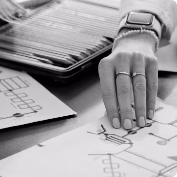 Close-up of two hands reviewing technical diagrams on paper, with a tray of drawing tools in the background.