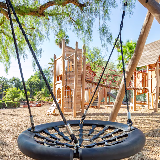 Close-up shot of a basket swing with a clear sightline showing a wooden climbing tower in the background at Sequoyah School in Pasadena, California