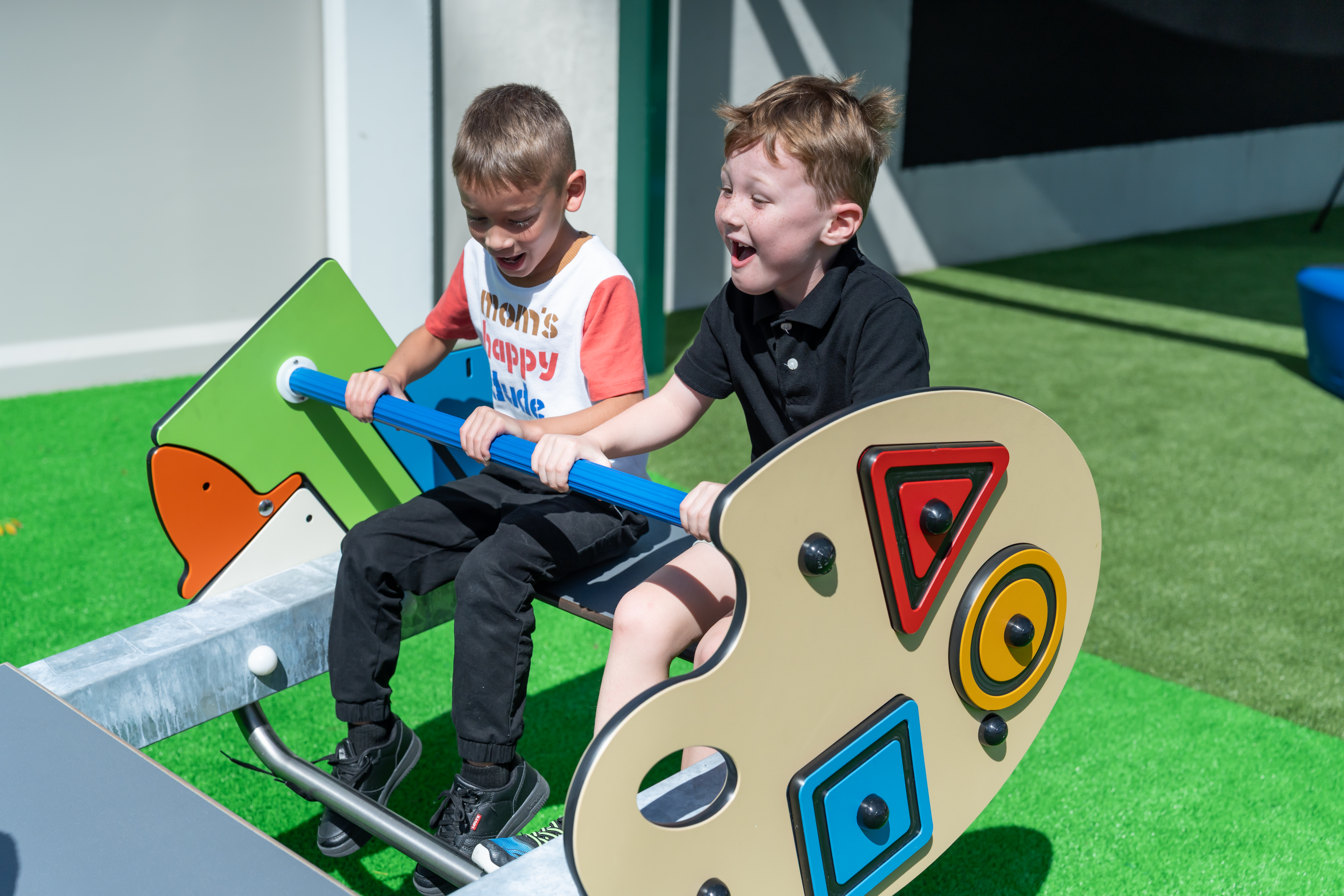 Two elementary-aged students playing on school playground equipment, featuring custom play panels, from KOMPAN