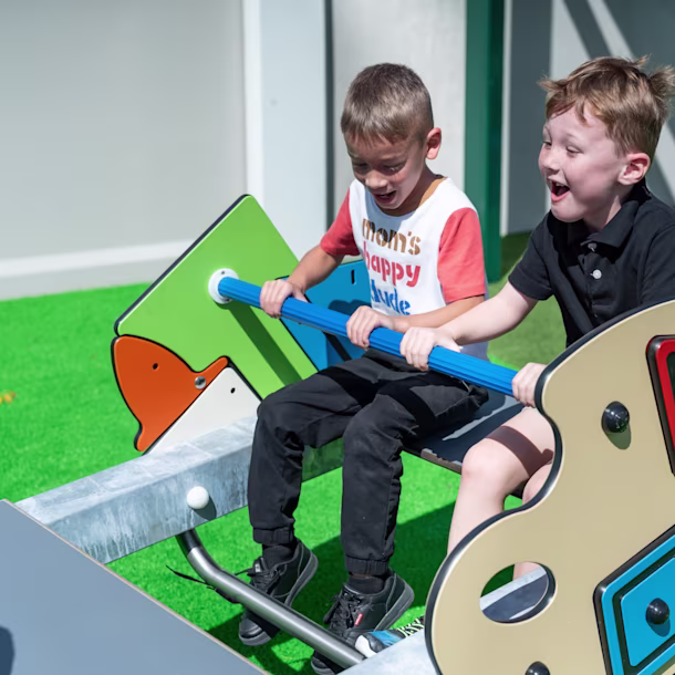 Two elementary-aged students playing on school playground equipment, featuring custom play panels, from KOMPAN