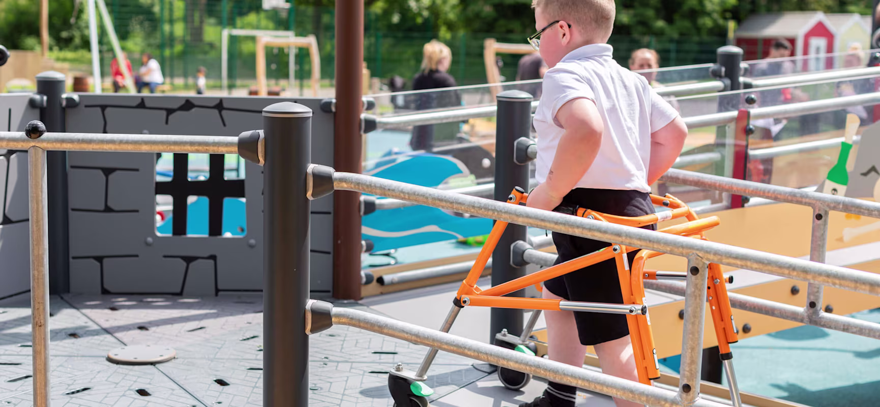 Junge mit einer Gehhilfe, der eine Rampe benutzt, um auf ein Spielgerät zu gelangen